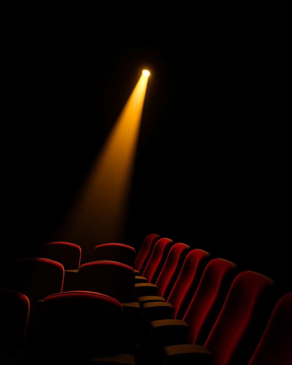 Rows of red-velvet theater seats under a single warm spotlight